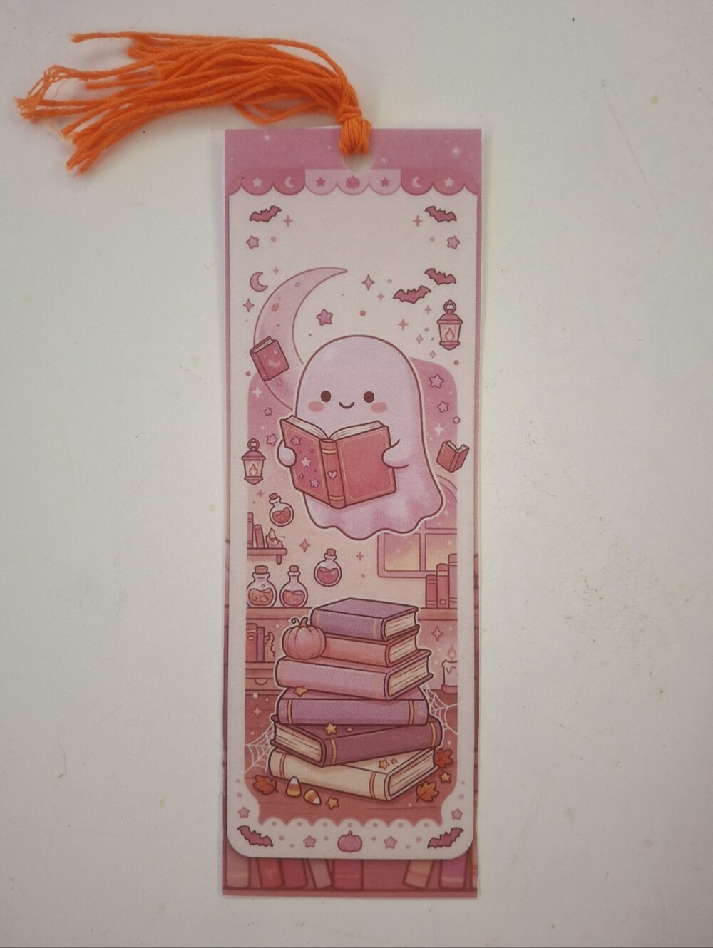 Pink ghost kawaii bookmark with cute ghost reading a book surrounded by books, b